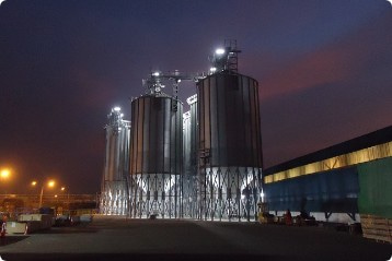 照明が各所に光り、巨大な4基の円柱状の構造物が並ぶ。夜間に撮影された飲料工場の写真