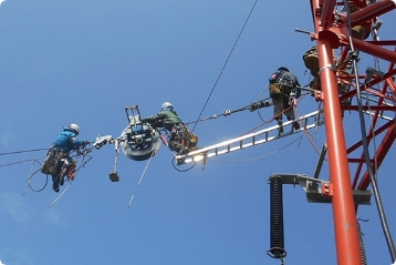光ファイバ工事の現場作業の様子を撮影した写真。数名の作業員が鉄塔の高所で作業を行っている